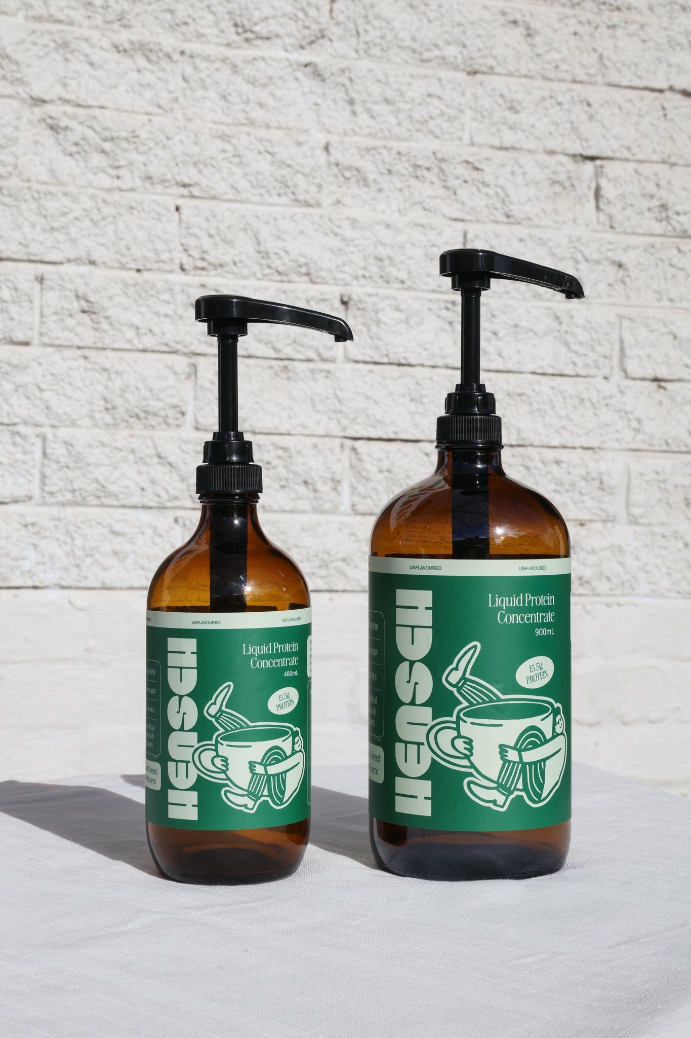 Two Hensch bottles with pumps against white brick